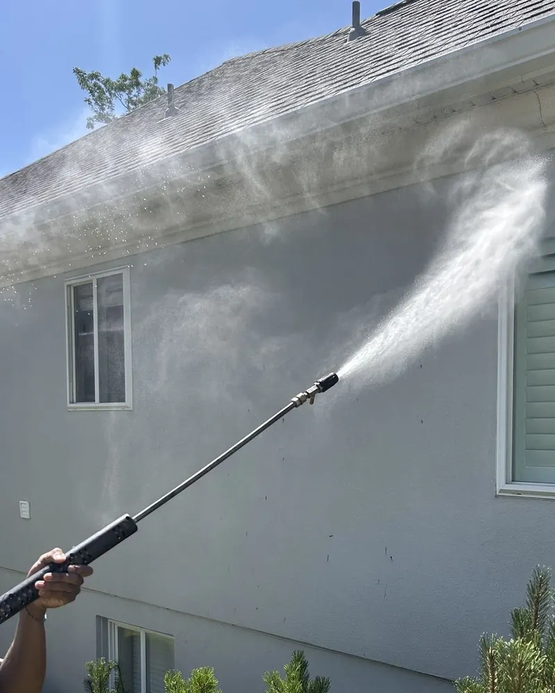 Lucent technician washing a roofline and gutter on a stucco home